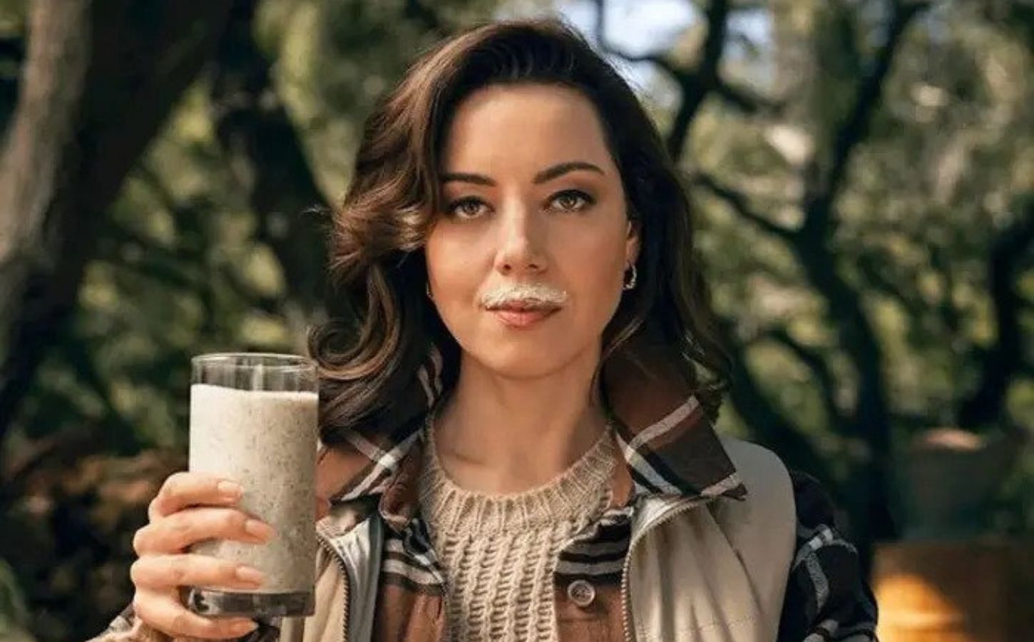 Actor Aubrey Plaza in a new satirical anti-vegan advert funded by the dairy industry, holding a glass of 'wood milk' with a milk mustache