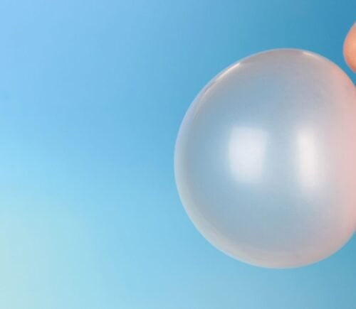 Photo shows part of someone's face (nose to chin) from the side as they blow a large pink bubble of chewing gum