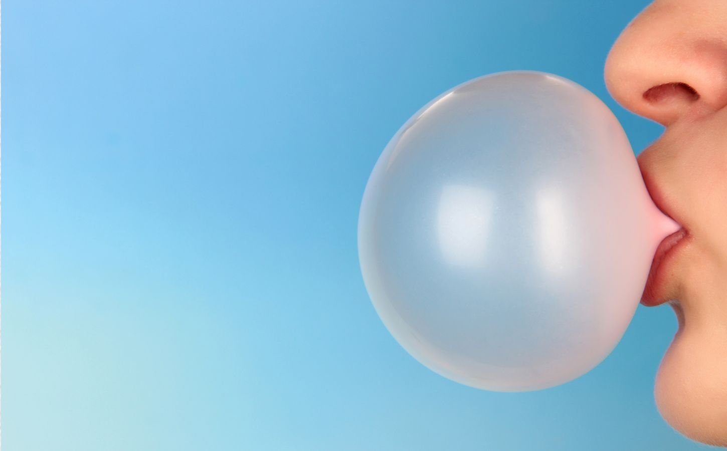 Photo shows part of someone's face (nose to chin) from the side as they blow a large pink bubble of chewing gum