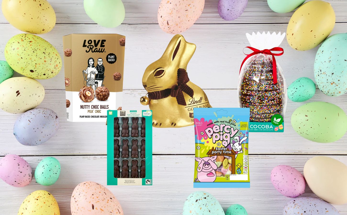 A range of vegan and dairy-free Easter chocolate and candy on a wooden plank backdrop, flanked by pastel Easter eggs