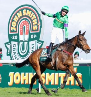 A person whipping a horse at the Grand National