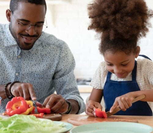 A child and her father cutting vegan food like peppers in the kitchen