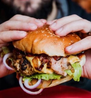 Photo shows a man's hands as he holds a meat-based burger up to the camera