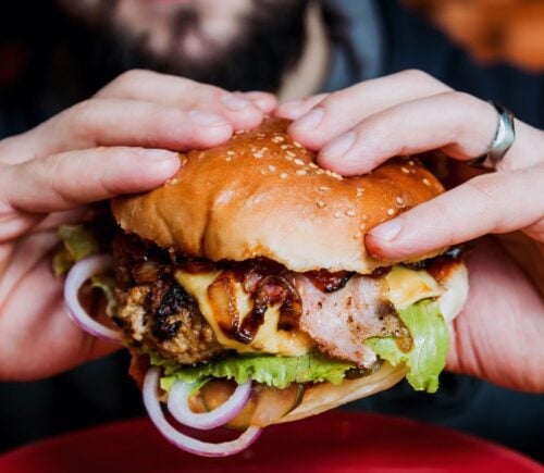 Photo shows a man's hands as he holds a meat-based burger up to the camera