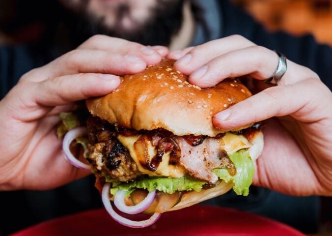 Photo shows a man's hands as he holds a meat-based burger up to the camera