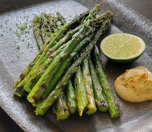 Grilled asparagus next to a portion of vegan lime miso mayo and a cut lime