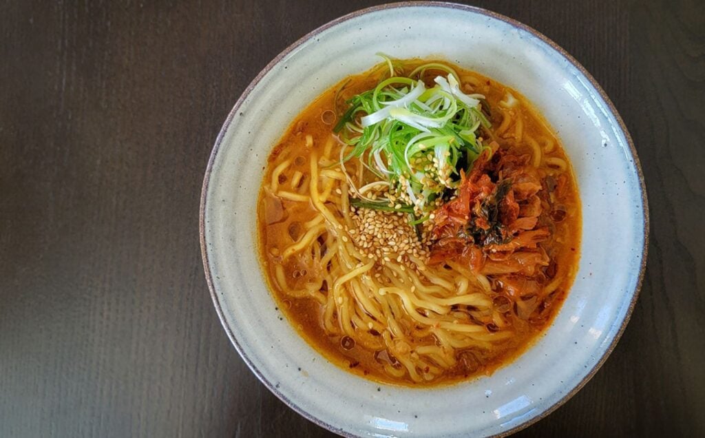 Freshly prepared vegan kimchi miso ramen in a white stoneware bowl, on a dark table