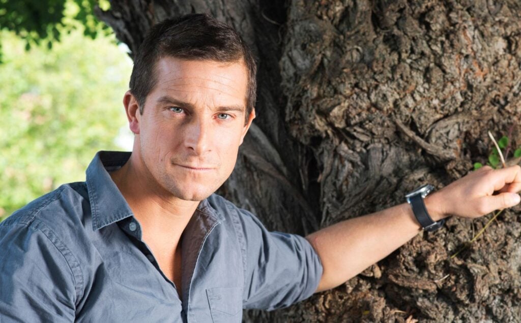 Bear Grylls, owner of an ancestral supplements brand that promotes the benefits of organ meat, resting his hand on a tree