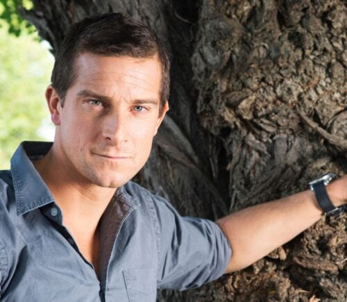 Bear Grylls, owner of an ancestral supplements brand that promotes the benefits of organ meat, resting his hand on a tree