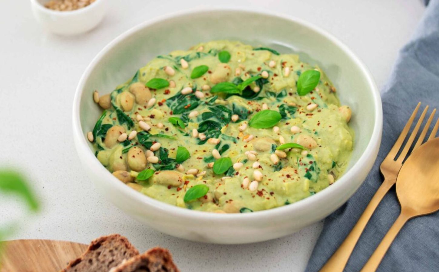 A bowl of vegan pesto butter beans next to some cutlery and bread