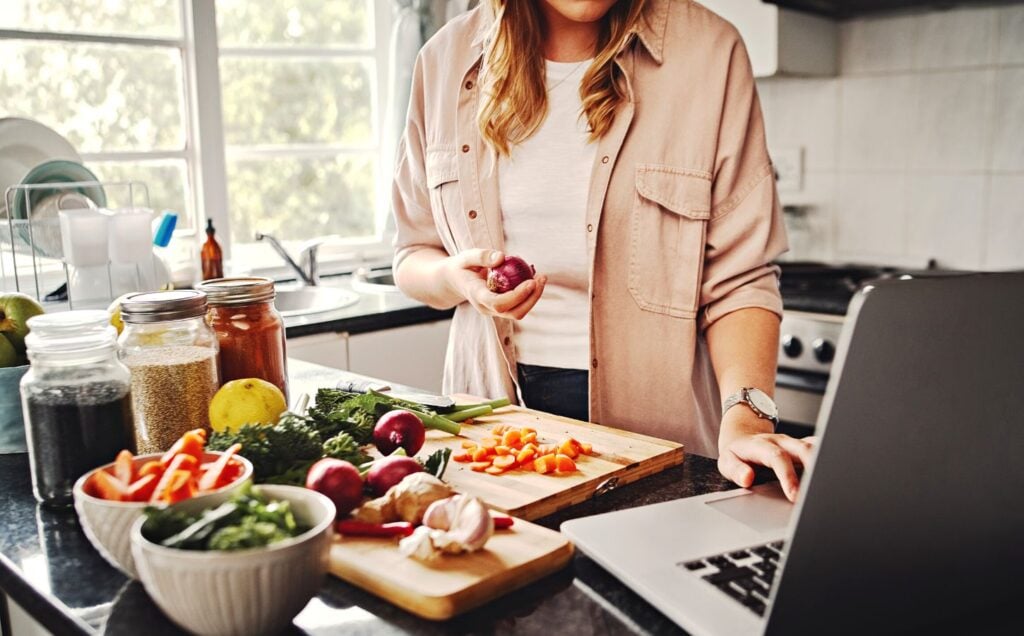 A woman preparing a meal in the kitchen using fruit and vegetables, essential for a healthy plant-based diet