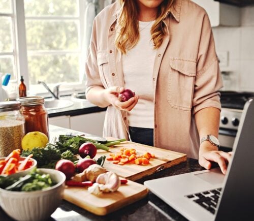 A woman preparing a meal in the kitchen using fruit and vegetables, essential for a healthy plant-based diet