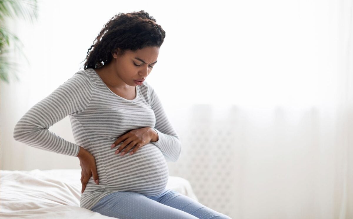 A pregnant woman sitting on a bed holding her bump