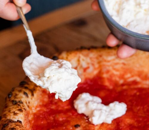 Close-up shot of vegan cheese being added to a plant-based pizza at Purezza