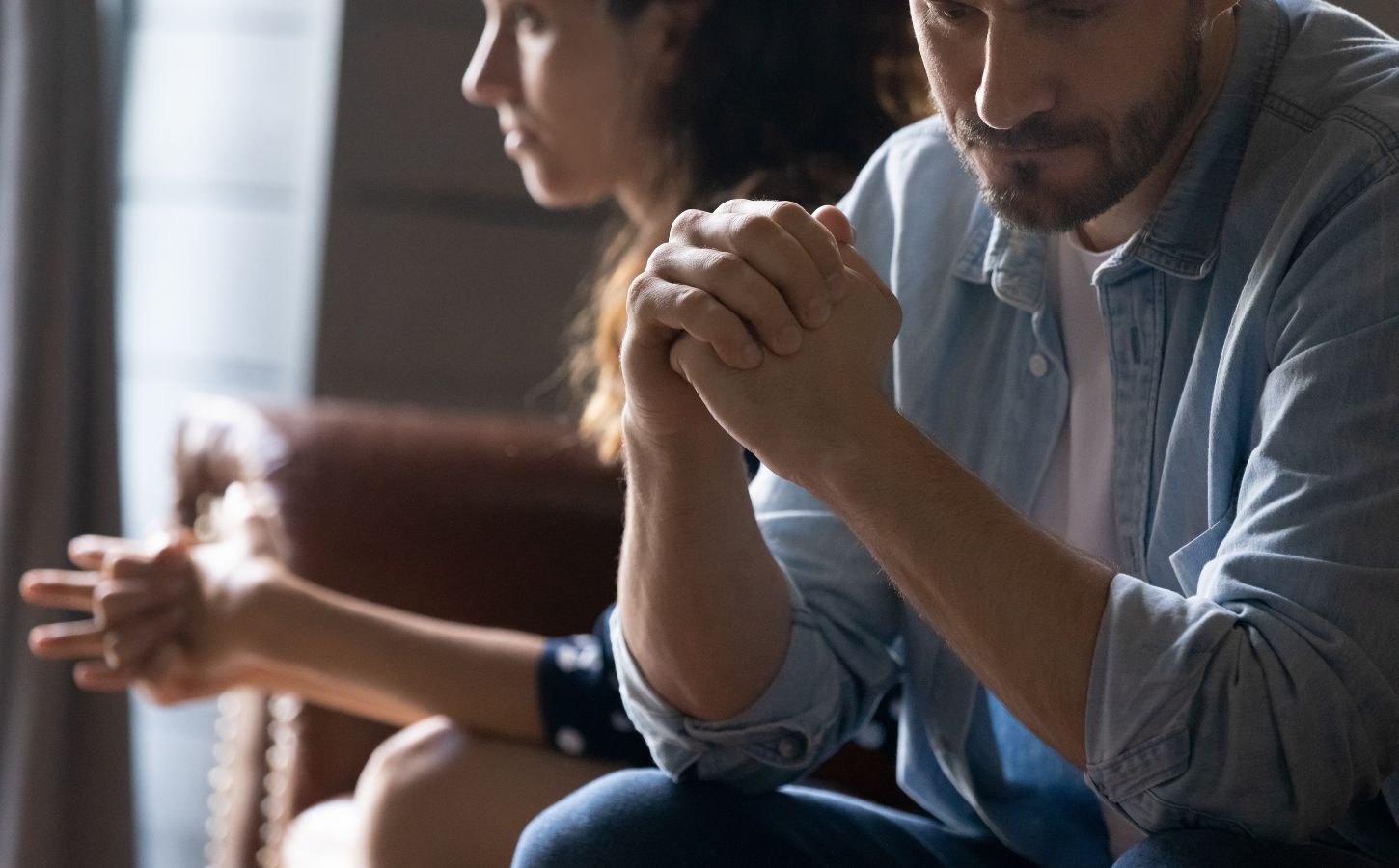 A couple in a relationship sit side-by-side, with one partner holding his fists in front of him