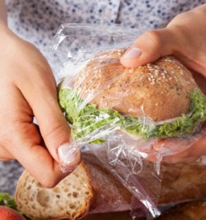 Photo shows someone's hands as they wrap a sandwich in a plastic Ziploc-style sandwich bag