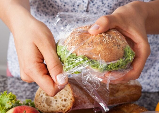 Photo shows someone's hands as they wrap a sandwich in a plastic Ziploc-style sandwich bag