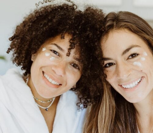 Two women with patches of natural skincare on their faces smiling at the camera