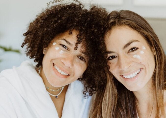 Two women with patches of natural skincare on their faces smiling at the camera