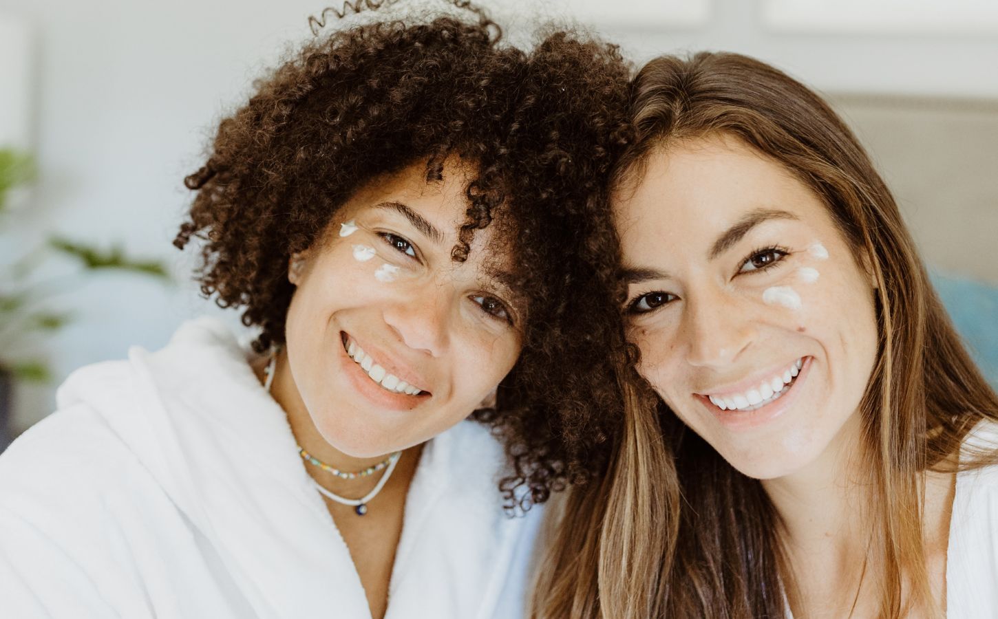 Two women with patches of natural skincare on their faces smiling at the camera