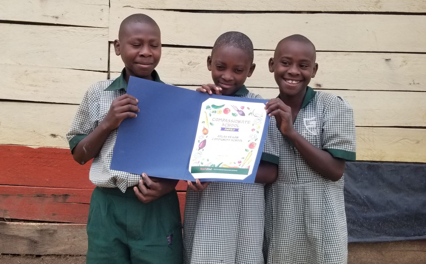 Three children from the Ugandan Atlas Community School in East Africa holding their TeachKind vegan award