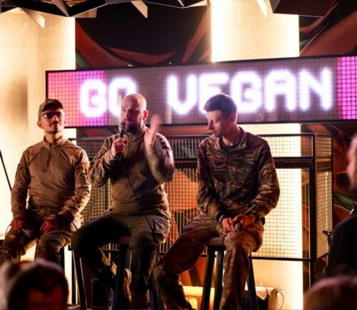 Soldiers on stage at a Ukraine vegan festival with the words "go vegan" on a screen behind them