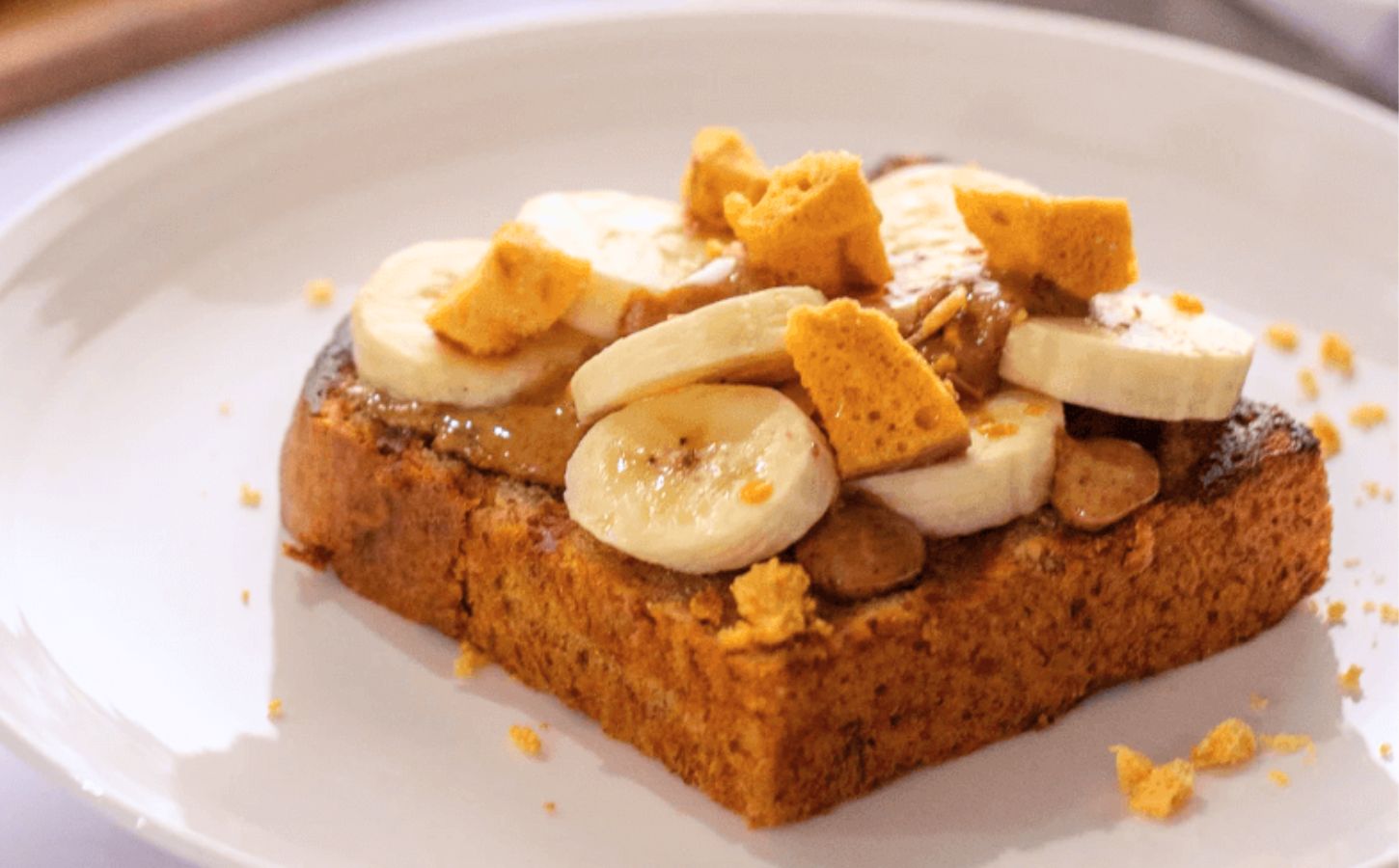 A slice of vegan banana bread topped with plant-based honeycomb, nuts, and slices of banana