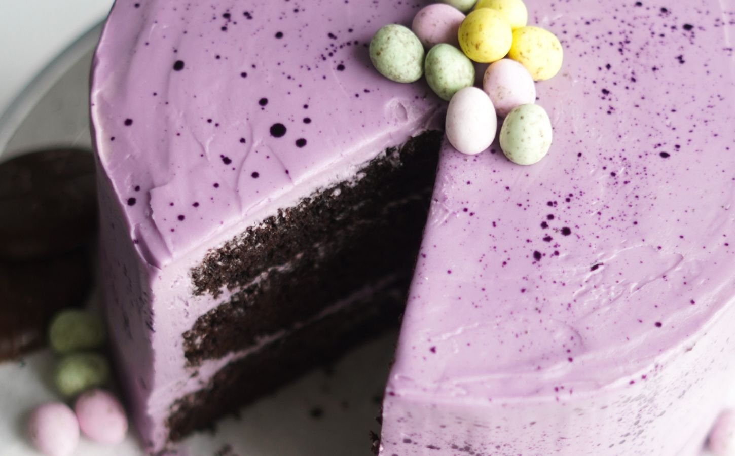 Moist vegan Easter chocolate cake with layers of purple vegan vanilla frosting and decorated with vegan mini eggs