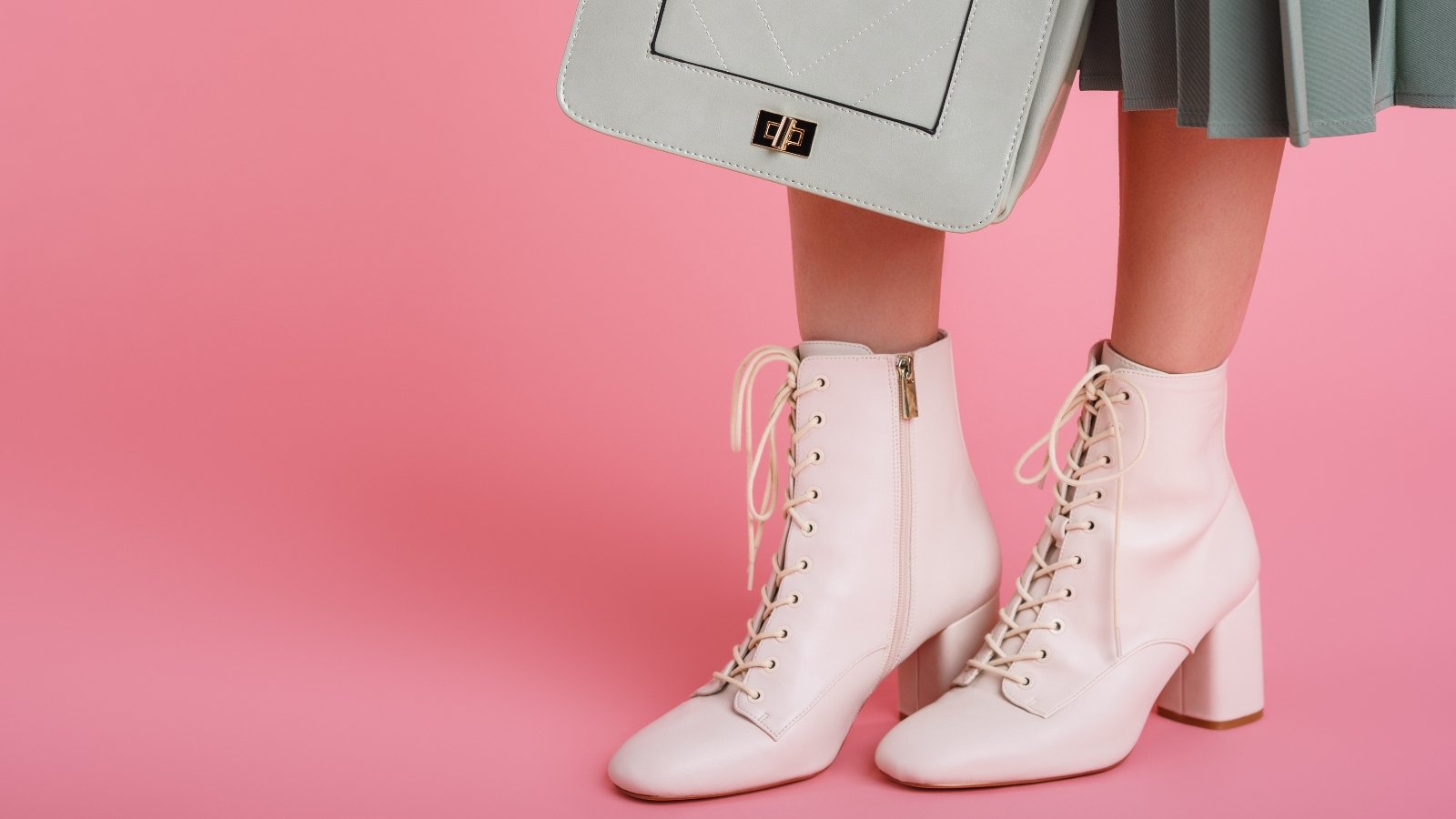 model wearing trendy white lace up ankle boots, holding stylish small green mint color faux leather bag, posing on pink background