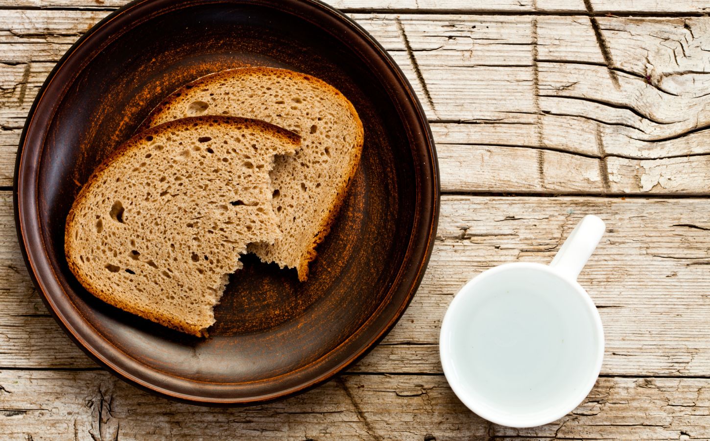 Two pieces of bread on a brown plate beside a white cup