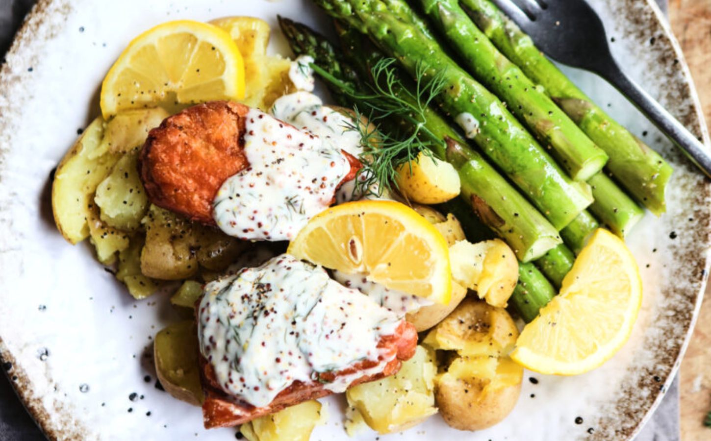 Vegan salmon fillets served with creamy dill sauce and vegetables on a white speckled plate