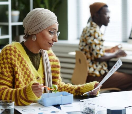 A woman sat at her desk at work eating a vegan meal