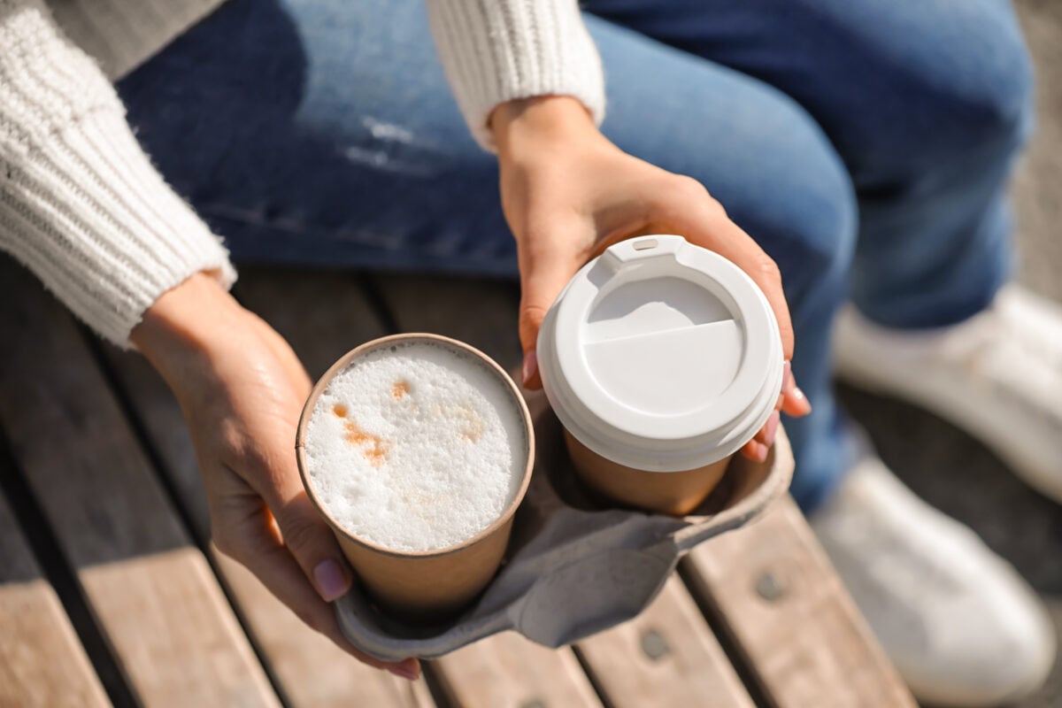 A person holding two takeaway coffees in disposable cups